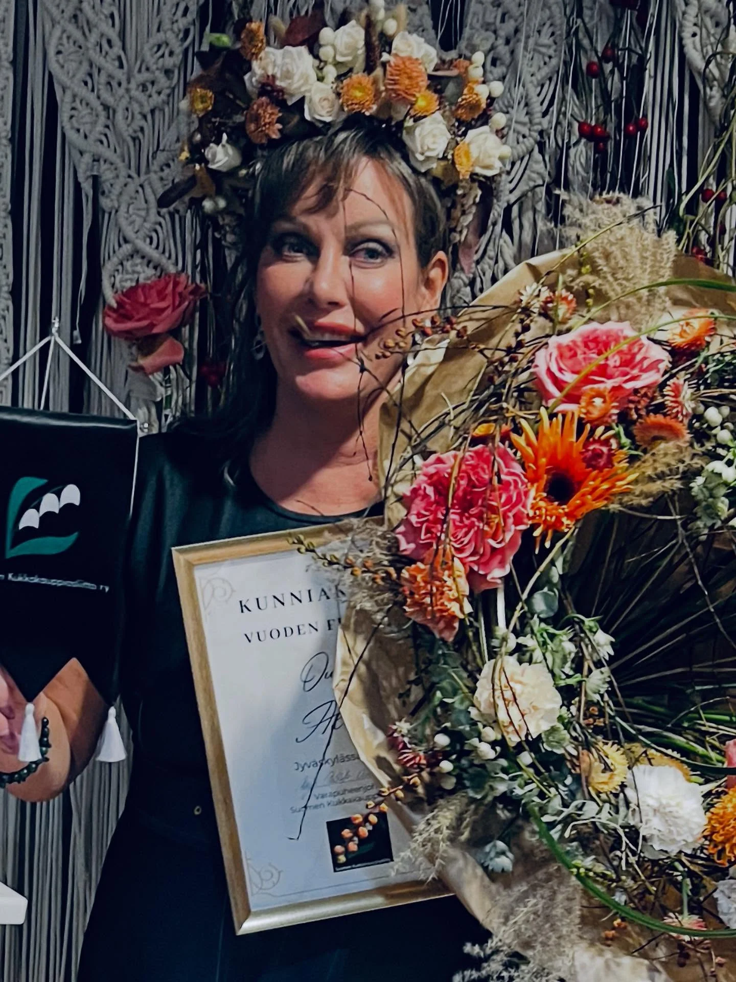 Floristi kukkien ja kunniakirjan kanssa taustalla runsas kukka-asetelma